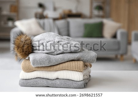 Stack of folded winter clothes with hat on table in room, closeup