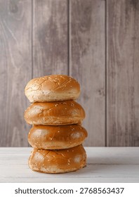Stack of four fresh burger buns with sesame seeds on a wooden background.