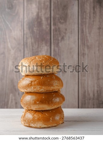 Stack of four fresh burger buns with sesame seeds on a wooden background.