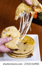 Stack of four fresh pupusas on a white square plate, traditional Salvadoran corn tortillas stuffed with cheese and beans.