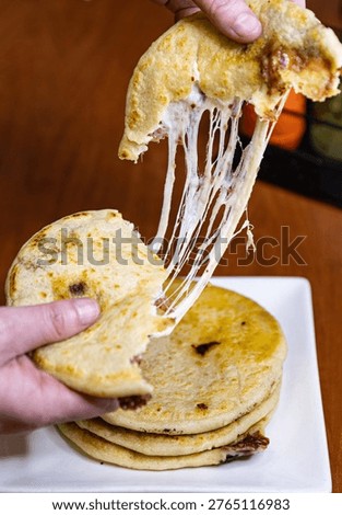 Stack of four fresh pupusas on a white square plate, traditional Salvadoran corn tortillas stuffed with cheese and beans.
