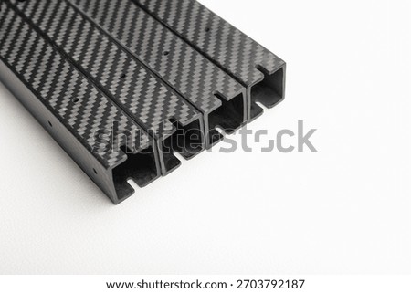 stack of four identical square-profile carbon fiber beams is diagonally placed on a clean white background.  lightweight composite parts arms for an FPV drone frame.