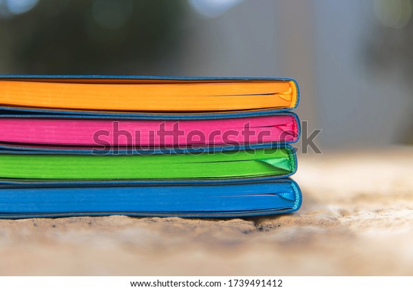 Stack of four notebooks with blue covers and\
fluorescent coloured pages piled on stone wall with satin ribbon\
page dividers visible