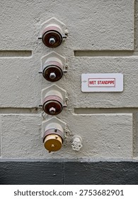 Stack of four wet standpipes with hydrant caps and sign on concrete wall