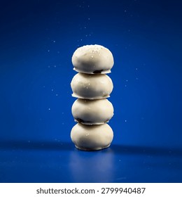 A stack of four white chocolate covered donuts with sprinkles on against a blue background with a few sprinkles scattered around.