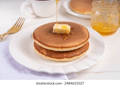 Stack of fresh baked homemade breakfast pancakes with butter and honey or maple syrup drizzles on white wooden table - Powered by Shutterstock