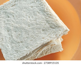 Stack of fresh crustless white bread slices on an orange plate, close-up view of soft bread texture.