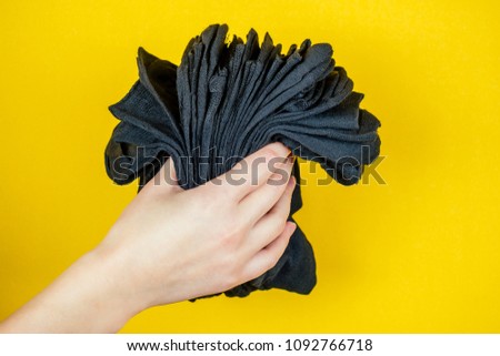 a stack of fresh new black socks in hand on a yellow background