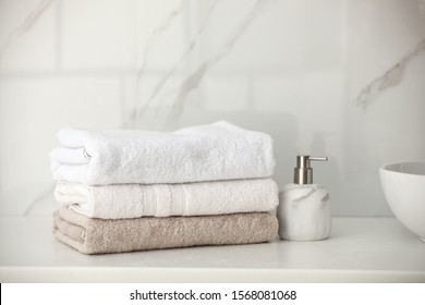 Stack of fresh towels and soap dispenser on countertop in bathroom
