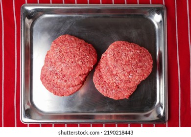 Stack Of Fresh Uncooked Beef Burgers On A Stainless Steel Metal Tray And On Red And White Stripe Butcher Apron. Meat Industry Product For Mass Consumption.