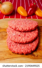 Stack Of Fresh Uncooked Beef Burgers On A Wooden Cutting Board And Red And White Stripe Butcher Apron. Meat Industry Product For Mass Consumption.