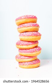 Stack of fresh yummy pink glazed donuts. Close-up. Doughnut day celebration. Homemade doughnuts with pink glaze and decorated with colorful confetti. Light background. 