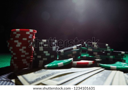 A stack of gambling chips, cards one hundred dollar bills on table.