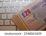 A stack of GBP British sterling pound bills on a computer keyboard