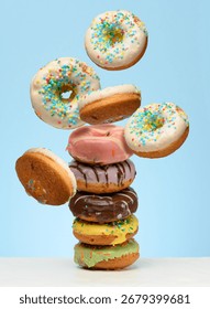 A stack  glazed donuts on a table. White donuts with sprinkles flying around them