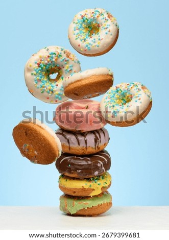 A stack  glazed donuts on a table. White donuts with sprinkles flying around them
