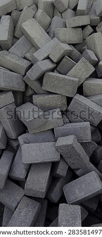 Stack of gray concrete paving blocks or bricks piled together. Used for road construction, sidewalk, and housing development in Indonesia. Building material and construction concept