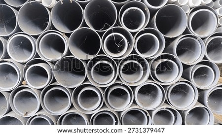 Stack of gray PVC industrial pipes with dust and cobwebs. Close-up background of plastic tubes for construction, plumbing, and drainage systems. Industrial texture and pattern.