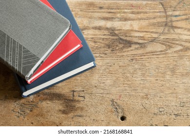 Stack Of Grey, Red And Navy Blue Books On A Rustic Vintage Desk, Close Up From Above With Copy Space