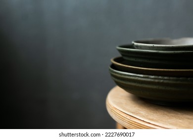 Stack of handmade ceramic craft ware - empty plates in natural colors on a wooden table. Selective focus. Grey background, copy space - Shutterstock ID 2227690017