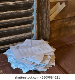 A stack of handwritten order slips pierced by a metal spike, placed on a rustic wooden counter near old wooden window shutters.