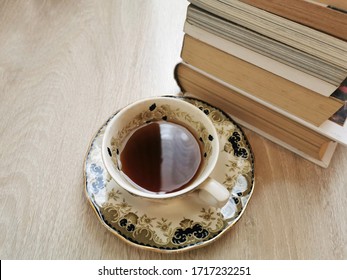 Stack of hardback books and a cup of tea in a vintage style on wooden floor. Selective focus.Landscape photo.