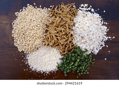 Stack of Healthy High Fiber Prebiotic Grains including wheat bran cereal, oat flakes and pearl barley, on rustic dark wood table background.