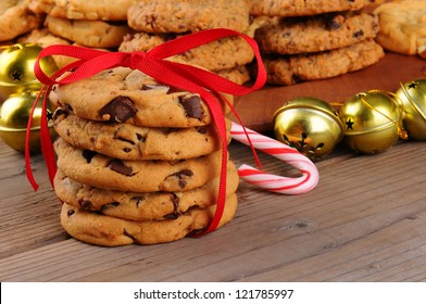 A stack of holiday chocolate chip cookies tied with a red ribbon in front of jingle bells , candy cane, and a platter of assorted baked treats. Horizontal format with shallow depth of field. - Powered by Shutterstock