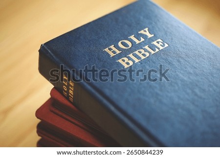 Stack of Holy Bibles with a close-up focus on the top blue Bible. Represents Christian scripture, religious faith, devotion, and spiritual study. Ideal for themes of worship.