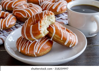 Stack of homemade baked pumpkin donuts with orange pumpkin glaze with bite in top donut sitting on white plate with cup of coffee