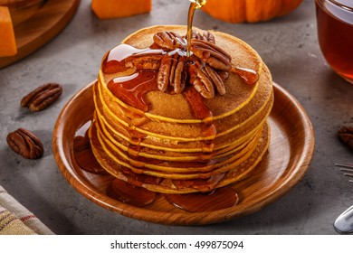 Stack of homemade pumpkin pancakes with pecans and maple syrup, selective focus.