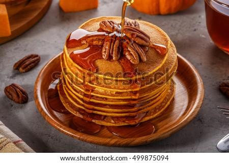 Stack of homemade pumpkin pancakes with pecans and maple syrup, selective focus.