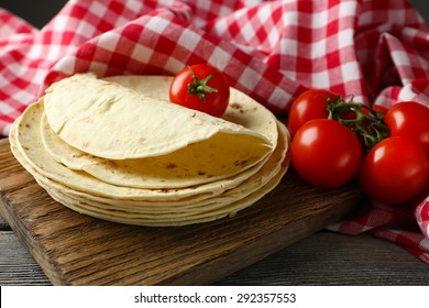 Stack of homemade whole wheat flour tortilla and vegetables on cutting board, on wooden table background