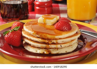 A Stack Of Hot Cakes With Syrup And Strawberries