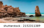 A stack of huge rocks on the sandy shore of blue sea