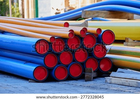 Stack of industrial plastic pipes with red protective caps on a city street. HDPE conduit for underground utilities at a construction site, Europe.