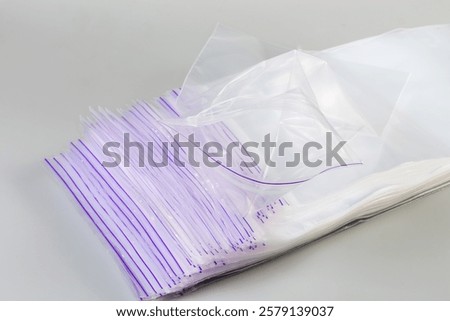 Stack of the inexpensive plastic rectangular transparent reclosable zip lock storage bags with mechanical sealing mechanism without slider on a gray background, close-up in selective focus