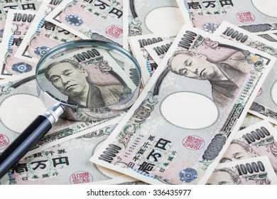 Stack of Japanese currency yen or Japanese banknotes with magnifying glass 