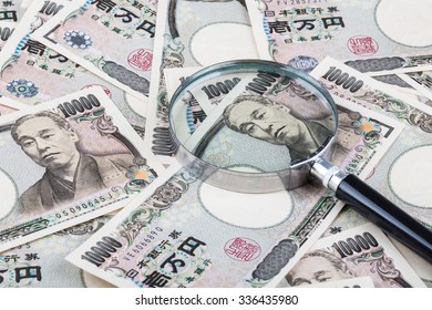 Stack of Japanese currency yen or Japanese banknotes with magnifying glass