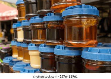 A stack of jars with different colored lids. The jars are filled with various types of honey