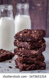 Stack of keto chocolate chip brownies with two bottles of milk against dark wooden wall