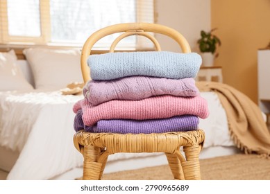 Stack of knitted sweaters on wicker chair in bedroom, closeup