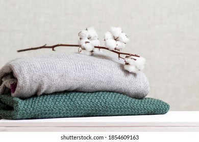 Stack of knitted warm clothes with cotton branch.