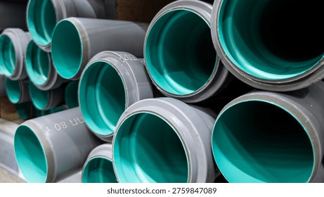 Stack of large grey PVC sewer pipes with teal green inner lining viewed from the open ends