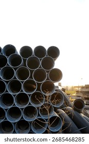 Stack of large plastic pipes arranged outdoors against bright sky, illustrating construction materials, industrial supply and urban infrastructure.