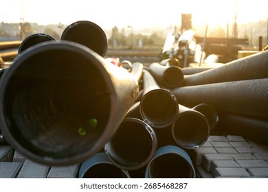 Stack of large plastic pipes arranged outdoors against bright sky, illustrating construction materials, industrial supply and urban infrastructure.