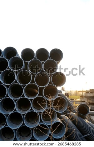 Stack of large plastic pipes arranged outdoors against bright sky, illustrating construction materials, industrial supply and urban infrastructure.