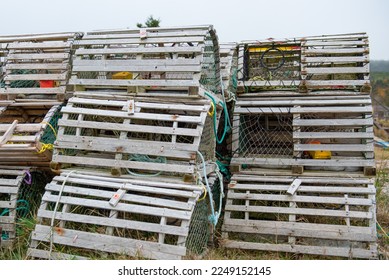 A stack of lobster pots sits on a local wharf out of water, waiting for the lobster fishing season to start. The traps are filled with weights and licenses. Some are square and some are round shapes. 