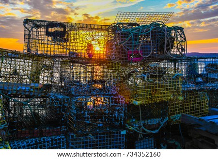 A stack of lobster traps and fishing equipment on a dock on Passamaquoddy Bay in Lubec, Maine, as the sun sets in the background