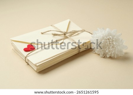 Stack of love letters, flower and red heart on beige background